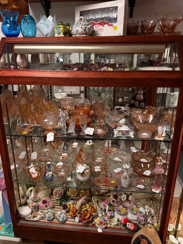 Pink glass and porcelain pieces arranged in a dealer display cabinet.